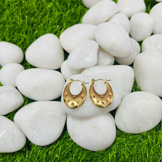 Gold hoop earrings on white pebbles with grass background