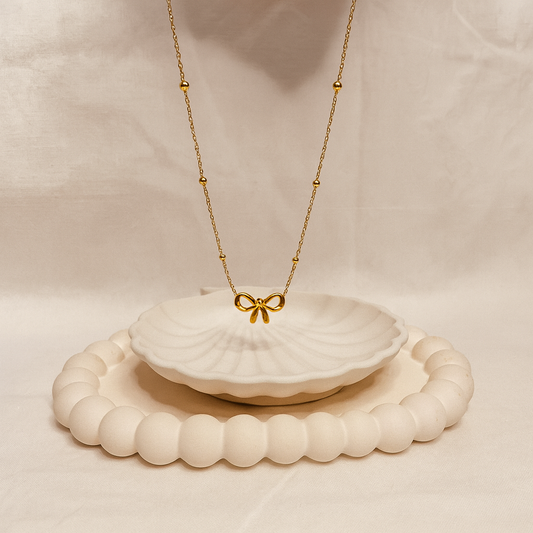 Gold necklace with a bow pendant on a white shell, placed on a beige surface.