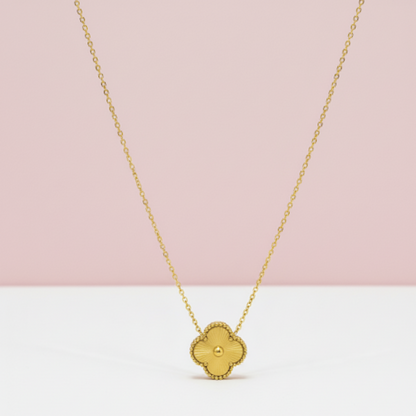 Gold necklace with a clover-shaped pendant on a pink and white background