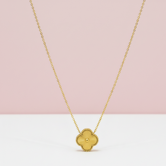 Gold necklace with a clover-shaped pendant on a pink and white background