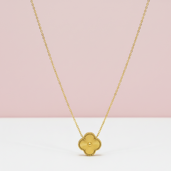 Gold necklace with a clover-shaped pendant on a pink and white background