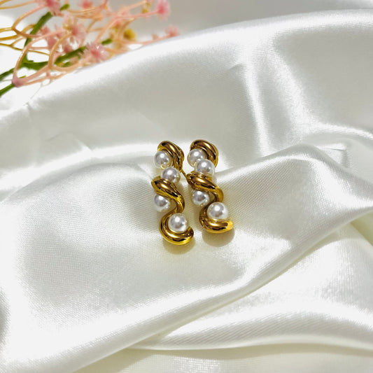 Gold pearl Twist earrings on a white satin surface with floral elements.