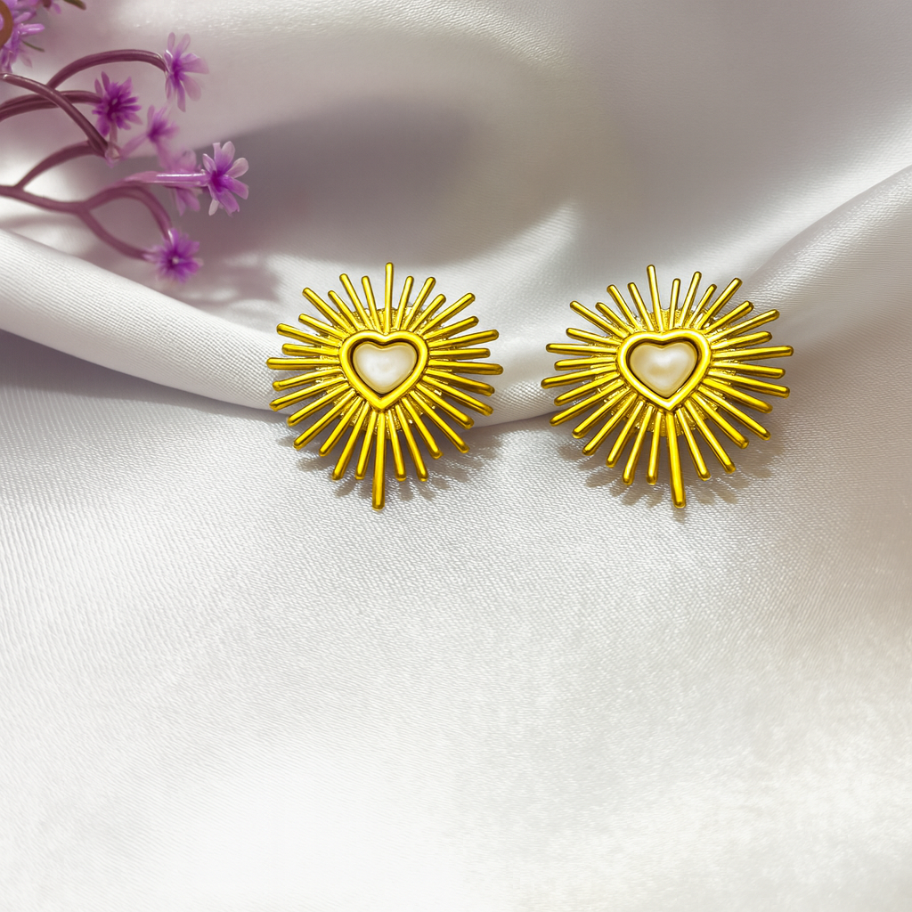 Gold sunburst earrings with a heart in the center on a white fabric background.