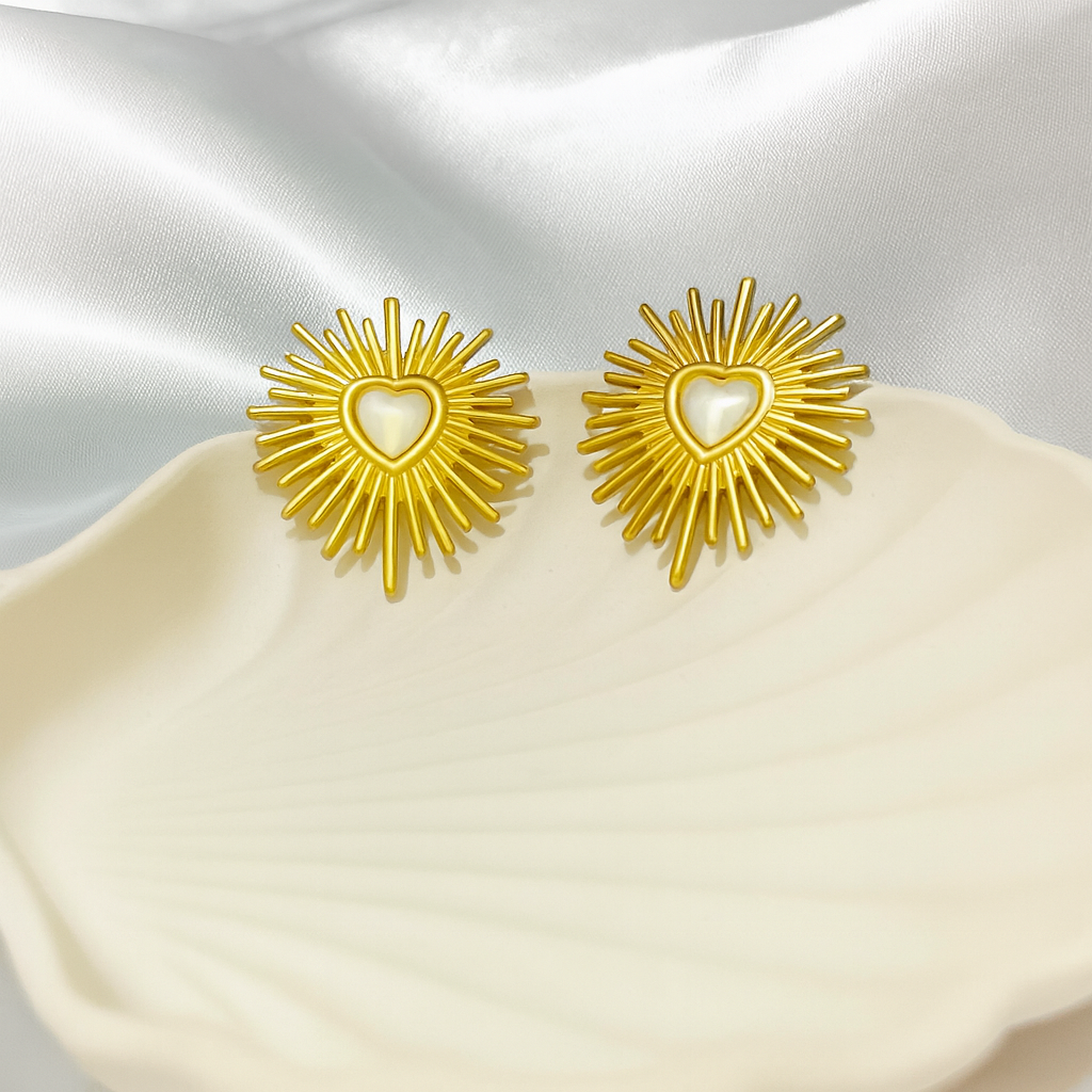 Gold sunburst earrings with heart center on a satin surface