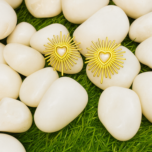 Gold heart-shaped earrings with sunburst design on white stones with green grass background
