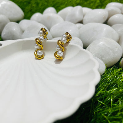 Gold and pearl earrings on a white dish with a natural background