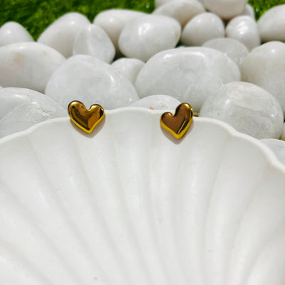 Gold heart-shaped earrings on a white shell with a natural background