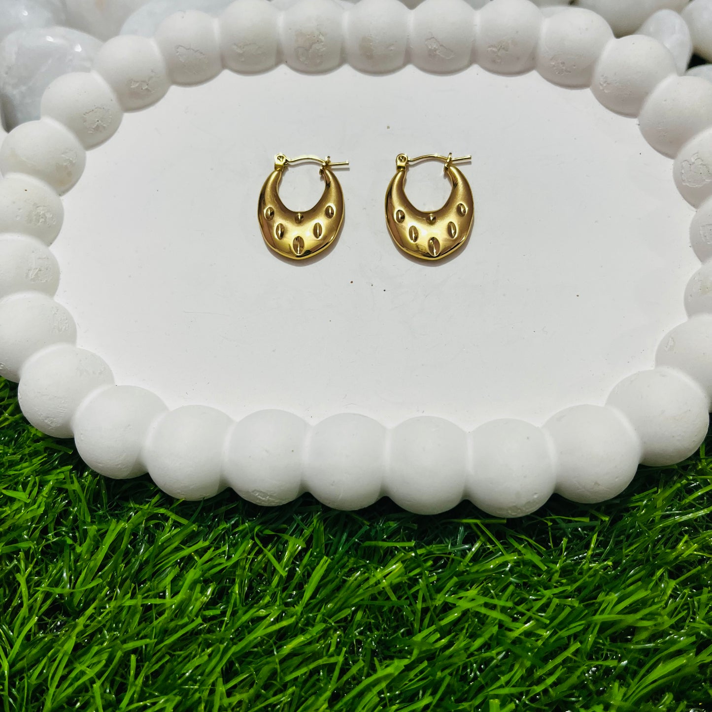 Gold hoop earrings on a white stone surface with grass at the bottom