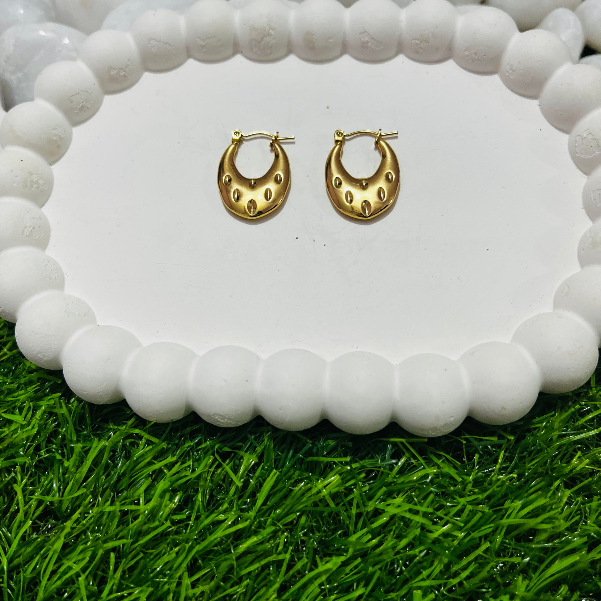 Gold hoop earrings on a white stone surface with grass at the bottom