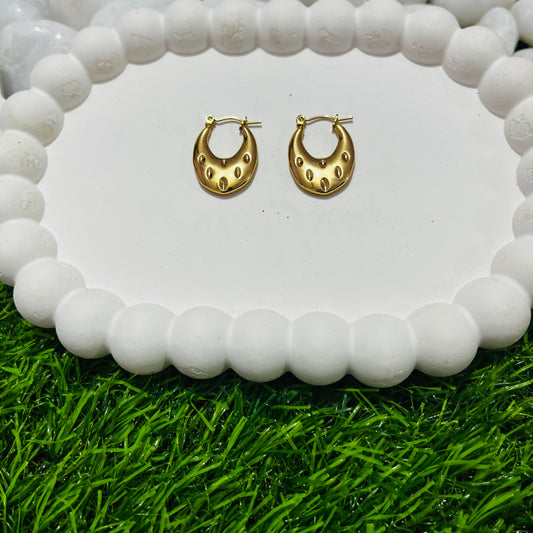 Gold hoop earrings on a white stone surface with grass at the bottom