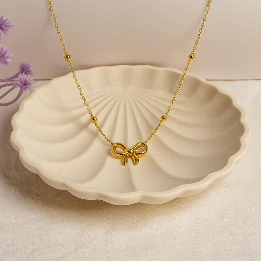 Gold necklace with a bow pendant on a ceramic dish