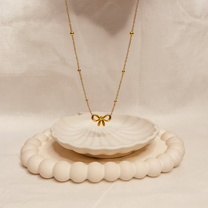 Gold necklace with a bow pendant on a white shell, placed on a beige surface.