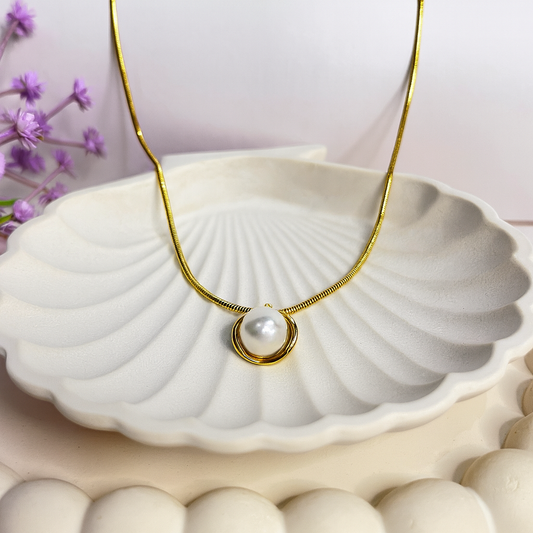 Gold necklace with a pearl pendant on a white shell with purple flowers in the background