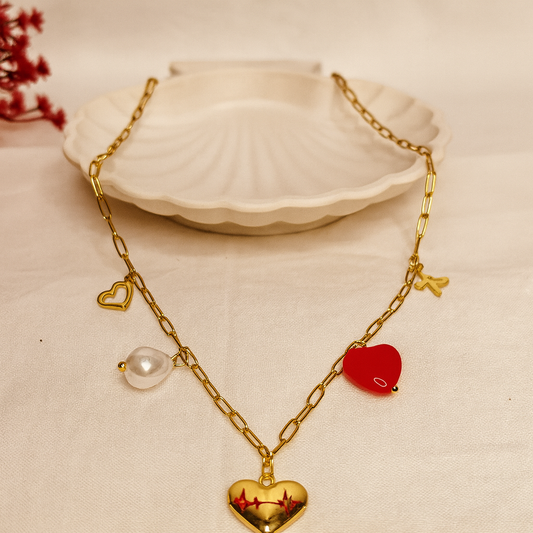 Gold necklace with heart and red apple pendants on a beige surface