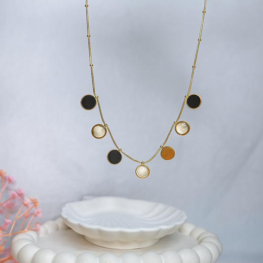 Necklace with circular pendants on a white dish against a light gray background